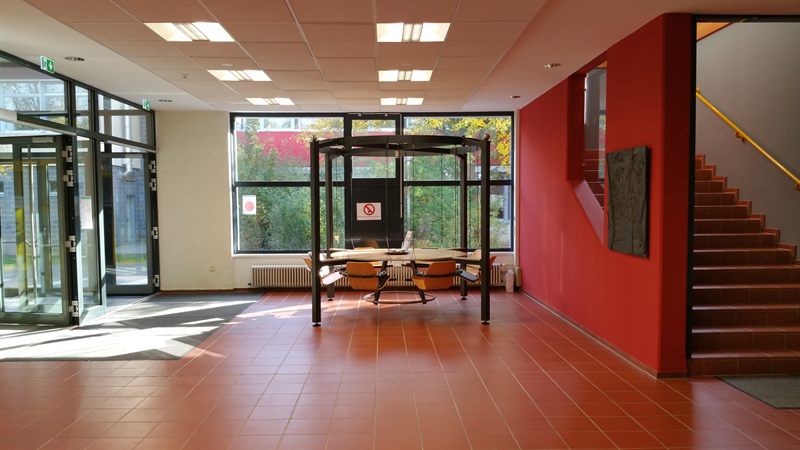 LOUNGETABLE in einem hellen Foyer mit roter Wand und Treppe